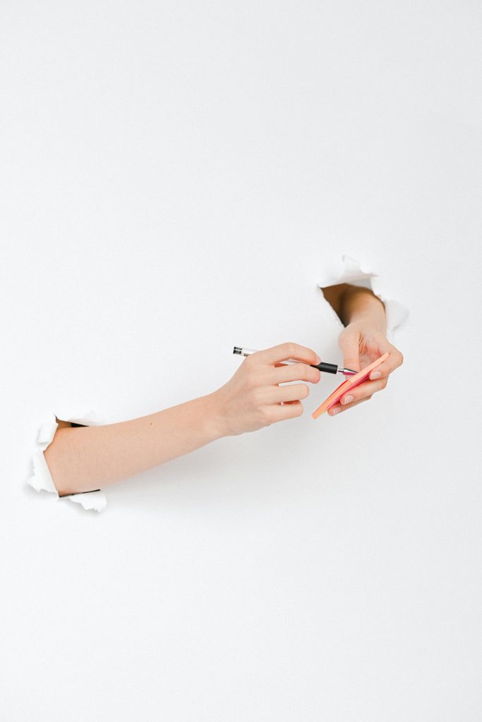 A Person's Hands Writing on a Sticky Note through a Hole